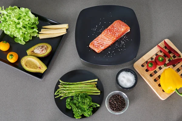 Top view of fresh Norwegian salmon steak  with organic vegetables on dark gray background - healthy food, diet or cooking concept.