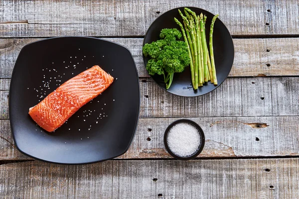 Top view of fresh Scottish salmon steak  with salt, asparagus and parsley on rustic wooden background - healthy food, diet or cooking concept.