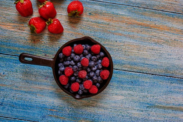 In the kitchen, bakery, cook pan left on the table with berries, side by side on a wooden table lie the few remaining strawberries