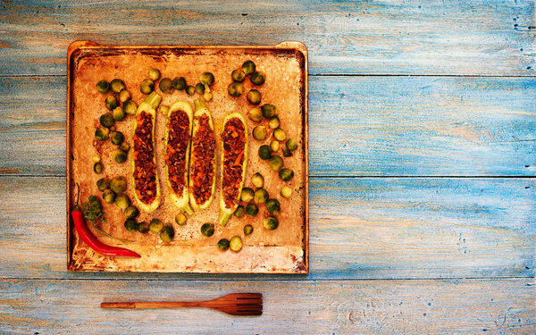 Housewife laid on a baking zucchini stuffed with minced meat, fried in a skillet until then, next to the zucchini expanded brussels sprouts as a garnish to the dish