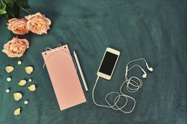 Smartphone ile çalışma alanı; Vintage kağıt mektup veya ileti; pembe yaprakları ve çiçekleri eski püskü mavi zemin üzerine; Kadın Danışma yaratıcılık için çalışmak; Pastel tonlu öğelerin natürmort; Üstten görünüm