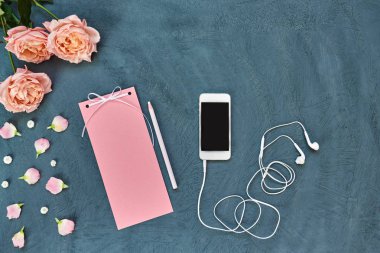 Çalışma alanı smartphone, vintage kağıt, mektup veya ileti, pembe yaprakları ve çiçekleri üzerinde eski püskü mavi arka plan ile. Kadın çalışma masası yaratıcılık için. Pastel tonlu öğelerin natürmort. Üstten görünüm.