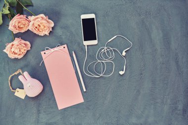 Çalışma alanı smartphone, vintage kağıt, mektup veya ileti, pembe yaprakları ve çiçekleri üzerinde eski püskü mavi arka plan ile. Kadın çalışma masası yaratıcılık için. Pastel tonlu öğelerin natürmort. Üstten görünüm.