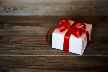 Beyaz hediye kutu kırmızı kurdele ve ahşap duvar arka plan kopya alanı ile yay ile sarılmış. Yılbaşı, Sevgililer günü, Doğum günü veya anneler günü tebrik için sunar. Tatil ambalaj kavram.