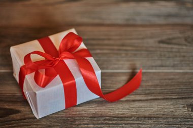 Parlak kırmızı saten şerit koyu ahşap rustik arka plan üzerinde beyaz el yapımı hediye kutusu. Kurdele ile yılbaşı, Sevgililer günü, Doğum günü veya yeni yıl için herhangi bir tatil kavramı sunar. 