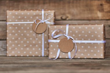 İki hediye kutuları kraft kağıt ve beyaz kurdele için Noel, Sevgililer, Doğum günü veya anneler günü tebrik için metin etiketi ile sarılmış. El yapımı hediye kutuları antika ahşap zemin üzerinde. Tatil kavramı.