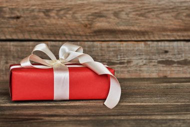 Kırmızı hediye kutusu beyaz kurdele ve ahşap duvar arka plan kopya alanı ile yay ile sarılmış. Yılbaşı, Sevgililer günü, Doğum günü veya anneler günü tebrik için sunar. Tatil ambalaj kavram.