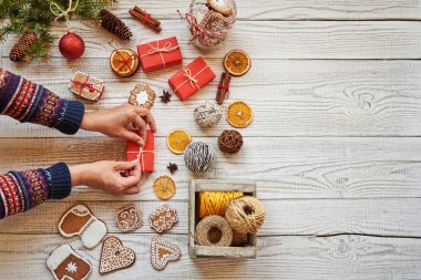 Kırmızı Noel hediye kutusu hediye ve süslemeleri ile beyaz ahşap masa üzerinde tutan kadın. Kopya alanı ile üstten görünüm.