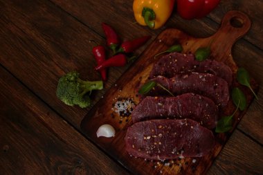 Sığır filetosu biftek ile baharat ve sebzeler ahşap tahta üzerinde. Bell ve biber biber, ot, tuz. Biftek hazır. dengeli beslenme, protein ve lif oncept. 