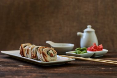 Füme yılan balığı, buzağı havyar ve peynir rulo zencefil ve wasabi görev yaptı. Lezzetli geleneksel Japon yemekleri beyaz porselen tabakta ahşap arka plan üzerinde suşi için. Sushi Menüsü. Seçici odak