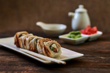 Füme yılan balığı, buzağı havyar ve peynir rulo zencefil ve wasabi görev yaptı. Lezzetli geleneksel Japon yemekleri beyaz porselen tabakta ahşap arka plan üzerinde suşi için. Sushi Menüsü. Seçici odak