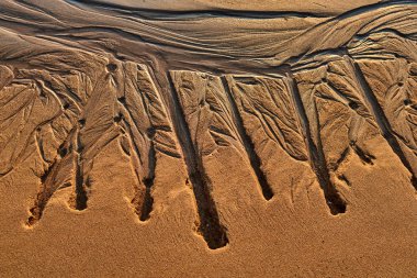 Dalgalar sahil kumu üzerinde izleri. Altın ışık ve gölge ile dalga tarafından izlenen sahilde kum.