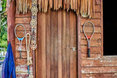 Eski ahşap cephe bir kamış çatı ve bir peeling kapı. Eski tenis raketleri bir eski püskü, ahşap duvar ve bir deniz ip üzerinde asılı. Grunge retro vintage house. Tozlu arka plan. 