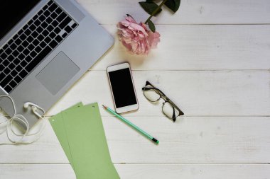 İletişim cihazları ile ev iş masası. Kadın Masaüstü boş yeşil kağıt, dizüstü bilgisayar, çiçek, smartphone ve gözlük. Eski püskü beyaz arka plan, kopya alanı, öğeler görünüm üst. Yukarı alay.