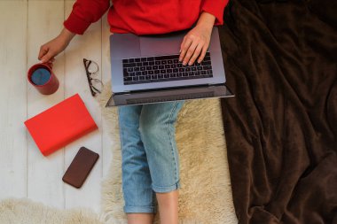 Üstten görünüm evde otururken dizüstü bilgisayar onun kucağına tutan genç bir kadın. Internet mağaza tarama için dizüstü bilgisayar kullanan kadın. Online alışveriş kavramı. Evde halı üzerinde oturan genç kadın