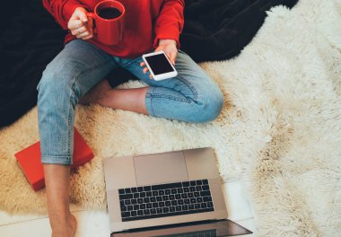 Laptop ve kahve Kupası ahşap bir katta oturan kızın elinde. Dizüstü bilgisayar, tablet ve kahve Kupası'nda rahat ev yazarak eller kadın. Üstten görünüm genç işkadını parlak modern iş istasyonunda oturan.
