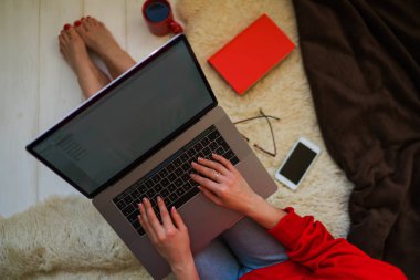 Üstten görünüm evde otururken dizüstü bilgisayar onun kucağına tutan genç bir kadın. Internet mağaza tarama için dizüstü bilgisayar kullanan kadın. Online alışveriş kavramı. Evde halı üzerinde oturan genç kadın