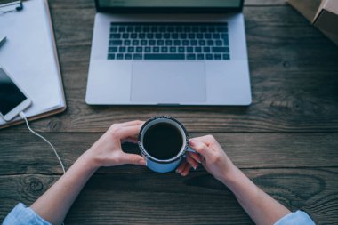 Üstten görünüm ofis masası. Kızın ellerini, dizüstü bilgisayar, kahve fincanı, smartphone ve defter ile çalışma alanı. Genç başarılı freelancer kadının elleri üzerinde taşınabilir klavye mesafe iş için dizüstü bilgisayar kullanmak.