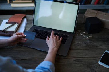 Kredi kartı numaraları evde tahta masada otururken bilgisayar Klavyede yazmaya tutan eller arkadan görünüş. Plastik kredi kartı ve dizüstü bilgisayar kullanarak elle. Seçici odak.