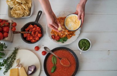 Domates soslu makarna masada kıyılmış peynir yağmurlama Cook'un el. Pasta malzemeler ile. Domates, sarımsak, maydanoz, biber ve parmesan peyniri Beyaz ahşap zemin üzerinde. Seçici odak. Üstten görünüm