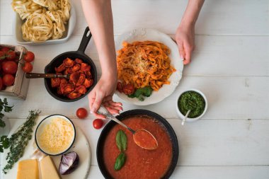 Profesyonel chef's pişirme makarna sebze, gıda katkı maddeleri ve mutfak eşyaları, üstten görünüm ile ahşap bir tezgah üzerine eller. Domates ve fesleğen plaka ve yemek pişirmek için malzemeler ile makarna. Gıda kavramı.