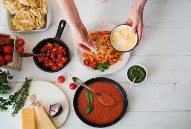 Domates soslu makarna masada kıyılmış peynir yağmurlama Cook'un el. Pasta malzemeler ile. Domates, sarımsak, maydanoz, biber ve parmesan peyniri Beyaz ahşap zemin üzerinde. Seçici odak. Üstten görünüm