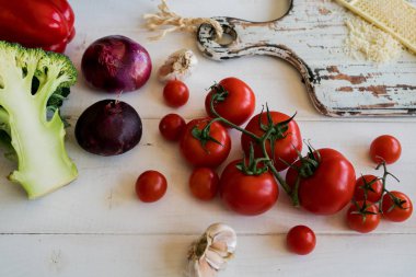 Domates, peynir, yeşil ve soğan taze vejetaryen yemek yemek. Sebze yemek yapmak için hazır. Ahşap kırsal masa ve malzemelerin üzerine açık renkli. Vejetaryen yiyecekler, kavram pişirme.
