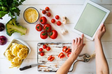 Yemek, mutfak, yiyecek, teknoloji ve insan kavramı. Mutfağında yemek için bir tablet bilgisayar kullanan genç kadın. Yemek menü arama ve pişirmeden önce gıda içerikler hazırlamak bir kadın.