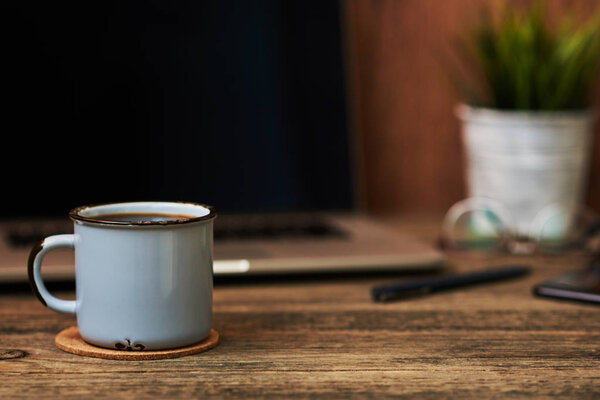 Workplace with close up cup of coffee, office supplies and laptop in the background. The blank screen can be used to put some text or images. Business concept with copy space. Vintage style