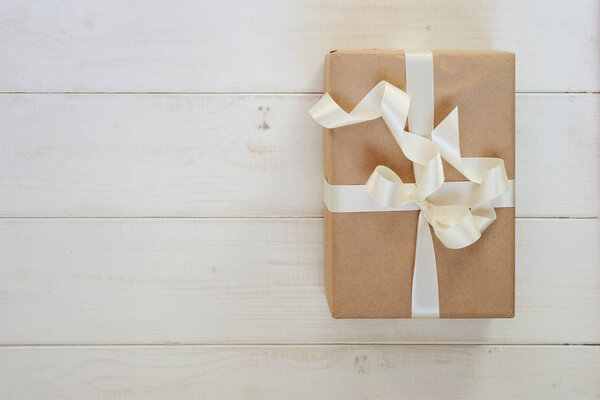 Ремесленная бумажная подарочная коробка ручной работы с блестящей белой атласной лентой на светлом деревянном деревенском фоне. Подарки с лентой на Рождество, День Святого Валентина, День рождения или Новый год для любой праздничной концепции
. 