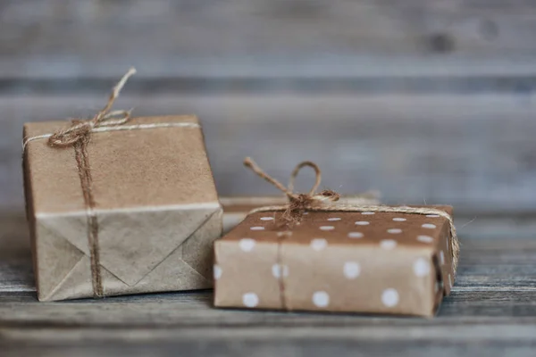 Boxes in craft paper, eco paper on the wooden table. Parcels or gifts tied with twine. Brown paper wrapped gift box with rope bow on a old rustic wood background. Background for your design.