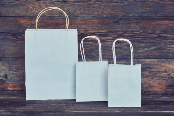 Mock-up of white craft paper package with handles, empty shopping bag with area for your logo or design, wooden board in the background, food delivery, sale, consumerism and advertising concept.