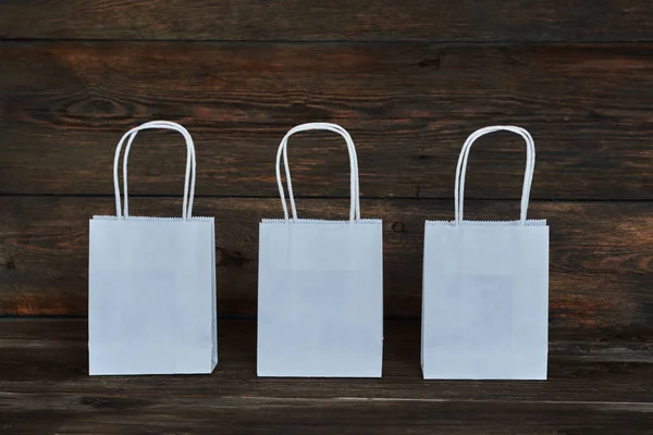 Mock-up of white craft paper package with handles, empty shopping bag with area for your logo or design, wooden board in the background, food delivery, sale, consumerism and advertising concept.