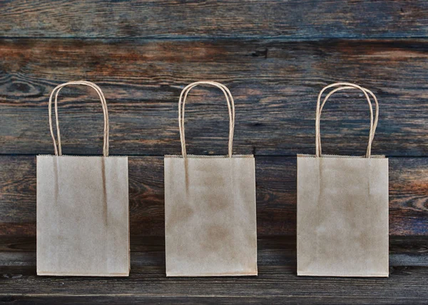 Mock-up of brown craft paper package with handles, empty shopping bag with area for your logo or design, wooden board in the background, food delivery, sale, consumerism and advertising concept.