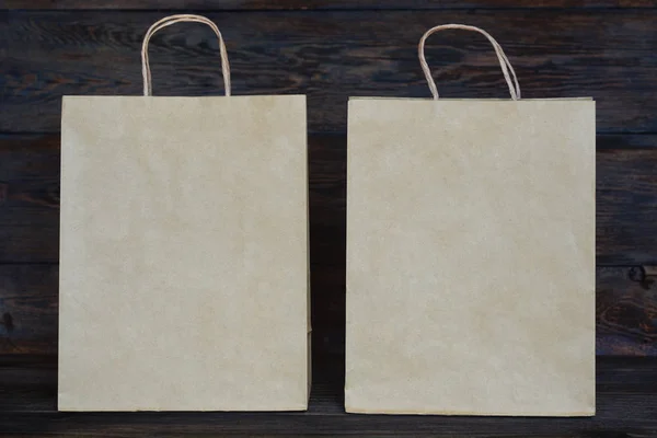 Mock-up of  brown paper package with handles, blank craft shopping bag with area for your logo or design, wooden board in the background, food delivery concept.