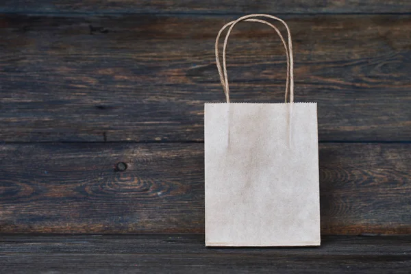 Mock-up of brown craft paper package with handles, empty shopping bag with area for your logo or design, wooden board in the background, food delivery, sale, consumerism and advertising concept.