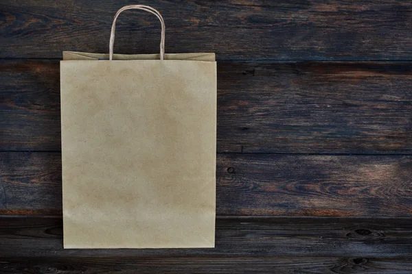 Mock-up of brown craft paper package with handles, empty shopping bag with area for your logo or design, wooden board in the background, food delivery, sale, consumerism and advertising concept.