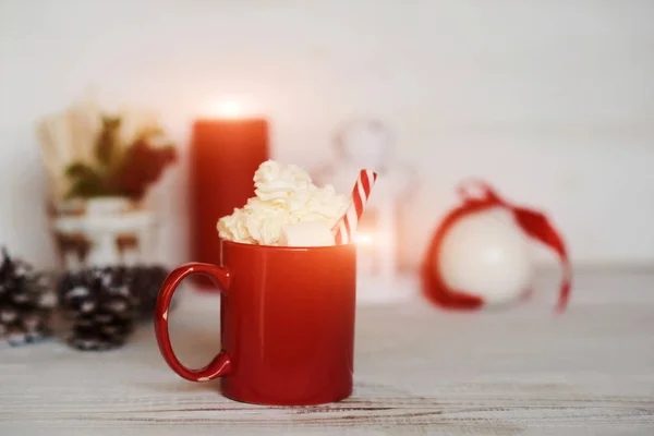 Red mug with hot chocolate with melted marshmallow and whipped cream. Winter hot drink. Christmas hot chocolate or cocoa with marshmallow on white background with christmas decorations.