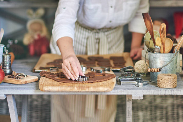 Women's hands making christmas cookies with metal cutter.