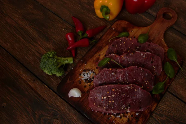 Sığır filetosu biftek ile baharat ve sebzeler ahşap tahta üzerinde. Bell ve biber biber, ot, tuz. Biftek hazır. dengeli beslenme, protein ve lif oncept. 
