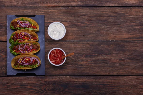 Taze sebze, marul ve zemin sığır eti kırmızı ve beyaz baharatlı sos ile ahşap masanın üzerinde yatan parçaları ile geleneksel Meksika börek