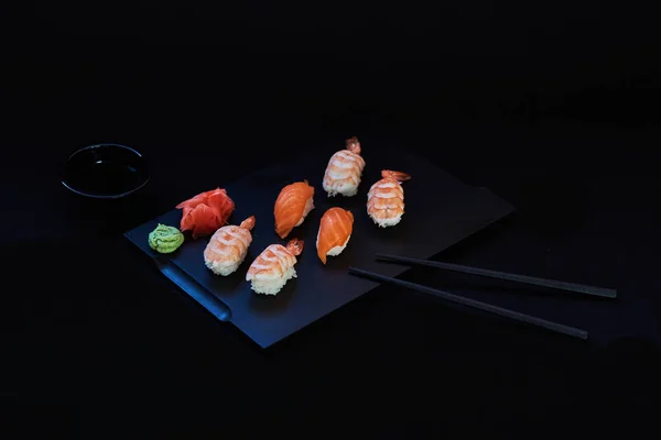 Sashimi sushi set on a black wooden board for sushi on black background. Close up of sashimi sushi with prawns. Traditional japanese food. Sushi menu. Delicious dinner in the restoran. Selective focus