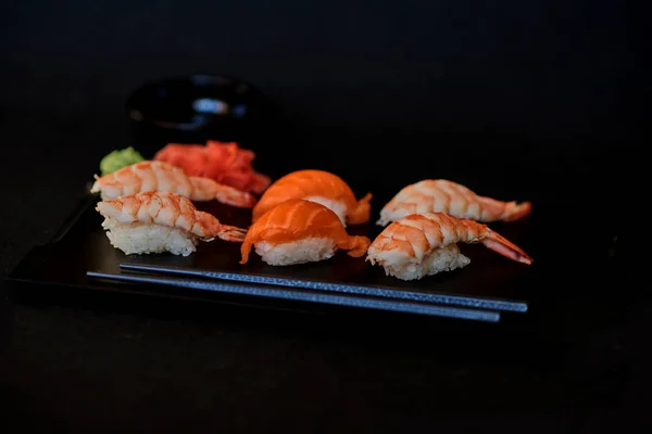 Sashimi sushi set on a black wooden board for sushi on black background. Close up of sashimi sushi with prawns. Traditional japanese food. Sushi menu. Delicious dinner in the restoran. Selective focus