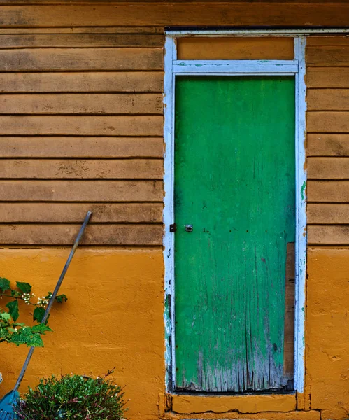 Old broken green shut door in an abandoned house with wooden panels and peeling cracked surrounding walls painted yellow. Abandoned facade with peeling yellow paint decaying facade
