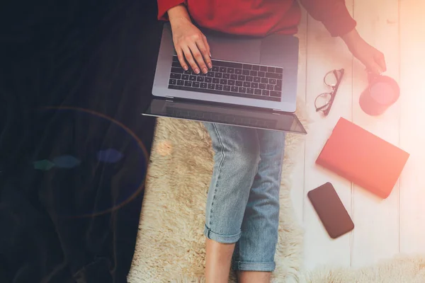 Young woman holding laptop computer on her lap while sitting at home. Woman using laptop for browsing internet store. Online shopping concept. Young woman sitting on carpet at home.