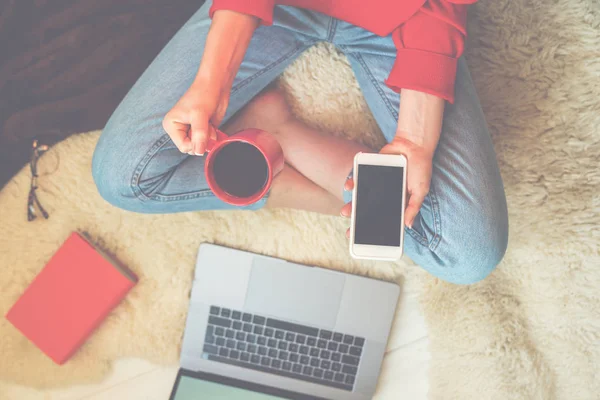 Top view of young woman sitting on floor with laptop. Enjoying time at home. Woman working on laptop and drinking coffee while sitting at home. Happy young woman sitting on the floor with crossed legs