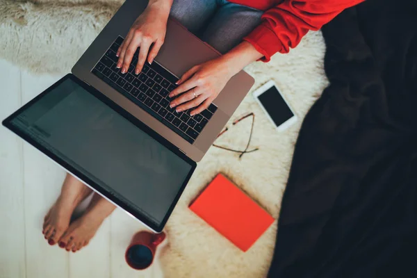 Young woman holding laptop computer on her lap while sitting at home. Woman using laptop for browsing internet store. Online shopping concept. Young woman sitting on carpet at home.