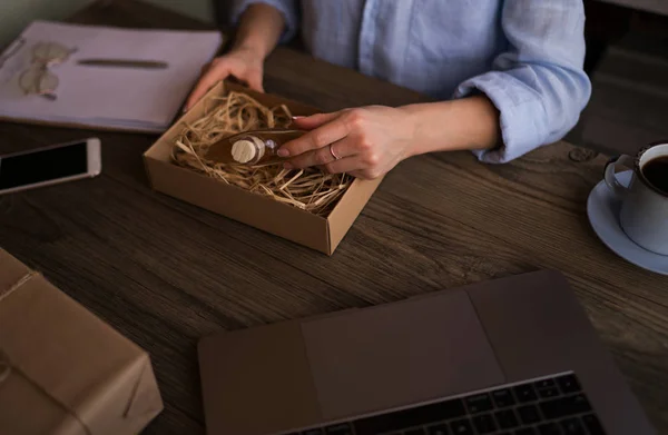 Woman makes online shopping or selling products in a room with laptop and brown box of items. Women working laptop computer from home on wooden desk with postal parcel. Selling online ideas concept.