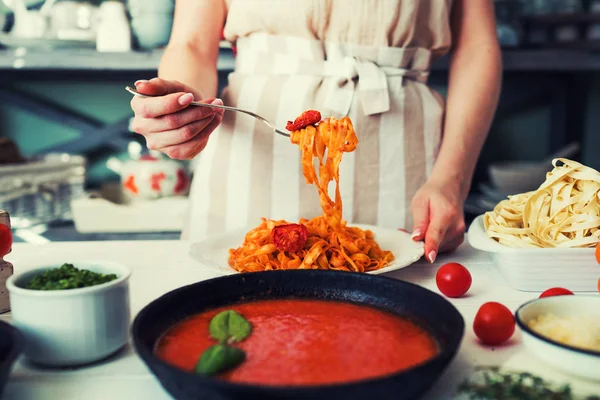 Italian style pasta dinner. Pasta with tomato and basil in plate on the wooden rustic table and ingredients for cooking. Chef hands preparing delicious pasta with tomato sous. Homemade food.