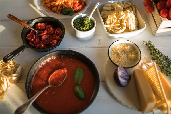 意大利面配辣番茄酱 干酪和罗勒 盘子里配有美味的面食 锅里有有机番茄酱和厨房木板的木桌 上面的景色 烹饪产品 软焦点 — 图库照片